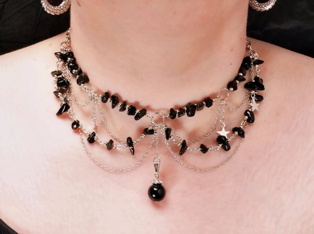 A multi-layered black necklace with natural pebbles and star charms, displayed on a model.
