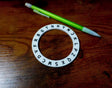 Circular object with letter labels on a wooden surface with a green pen.