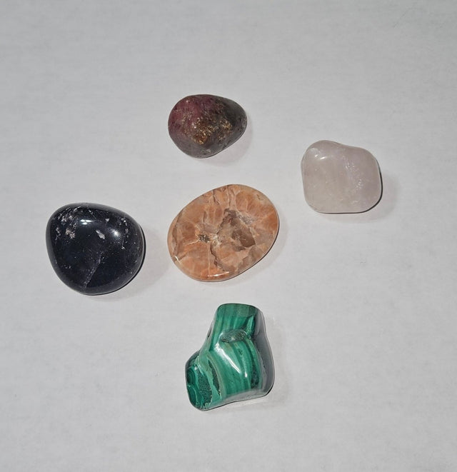 Five different colored stones on a white sheet of paper with a wooden surface underneath.