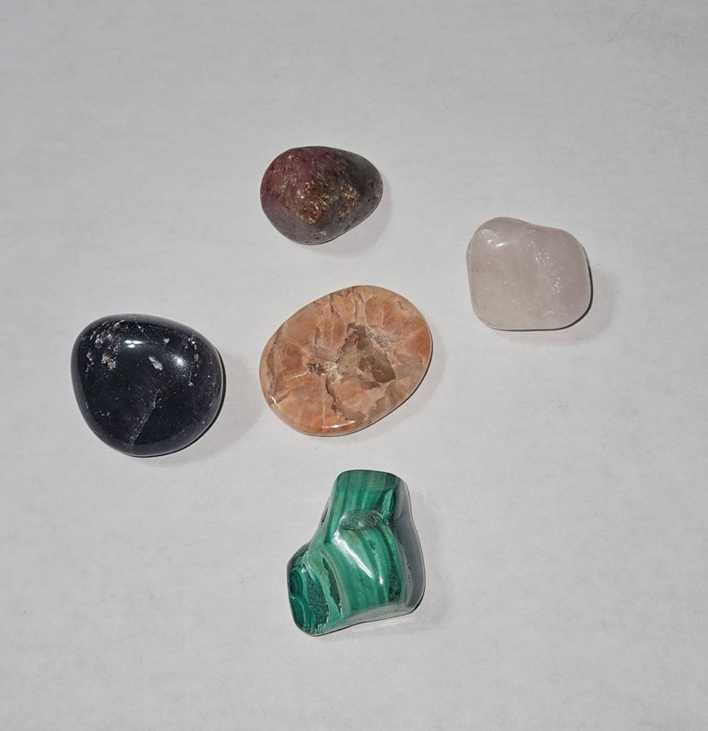 Five different colored stones on a white sheet of paper with a wooden surface underneath.