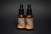 Two bottles of Locifer Ritual Oil with botanicals on a dark background