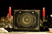A gothic-style handbag designed to resemble a spellbook, featuring a crescent moon and pentacle symbols. The bag is displayed with candles and a dark backdrop, emphasizing its mystical and elegant design.