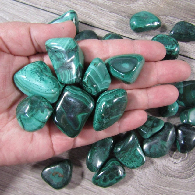 Hand holding green malachite stones on a wooden surface