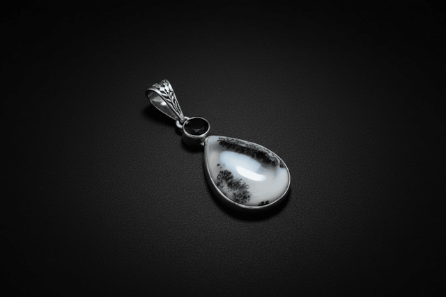 Representative front view of a pendant sold as Merlinite or dendritic opal with black spinel accents and supplier-listed sterling silver; identities, treatment, pattern, metal fineness, selected shape, and exact condition vary