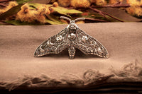 A silver moth hair clip with moon phase designs on its wings, displayed on a textured background.