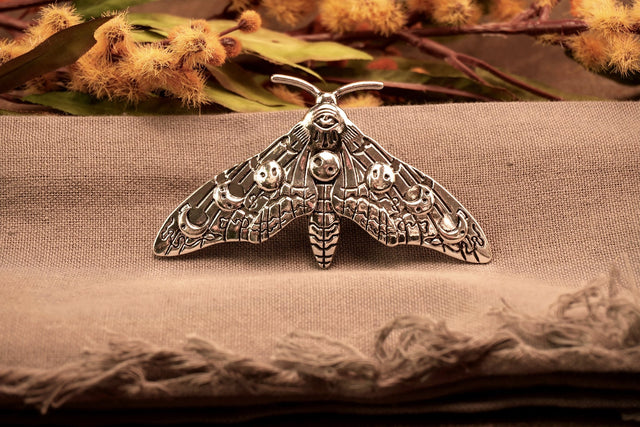 A silver moth hair clip with moon phase designs on its wings, displayed on a textured background.