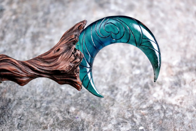 A resin wand with a woodgrain appearance, twisted tip, and a blue crescent moon design at the top. It also features a sculpted wrap of resin cloth on the handle.