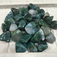 Collection of green and gray tumbled stones on a wooden surface