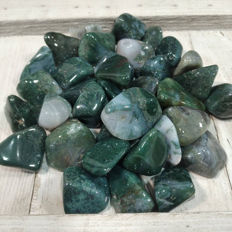 Collection of green and gray tumbled stones on a wooden surface