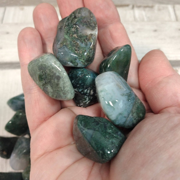 Hand holding several green and gray marbled stones against a white tiled background