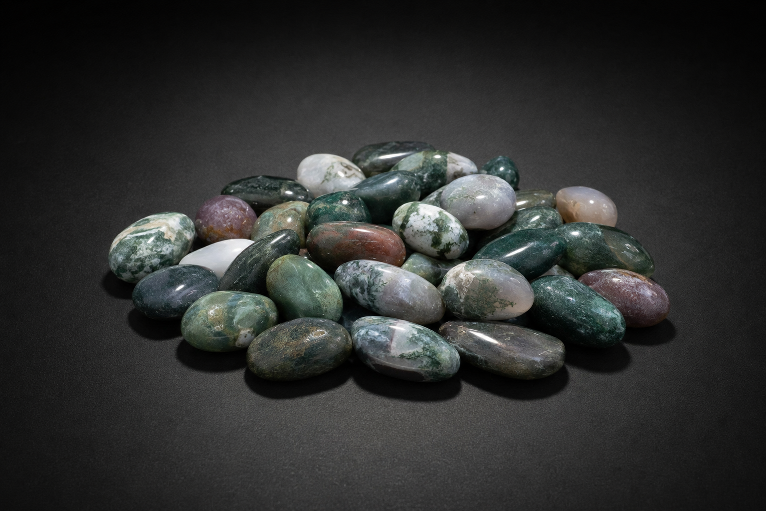 Assortment of polished Moss Agate stones with green, white, gray, brown, and mauve patterning on black
