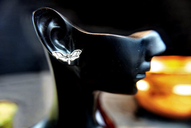 Black earring with butterfly design on a mannequin ear against a blurred background
