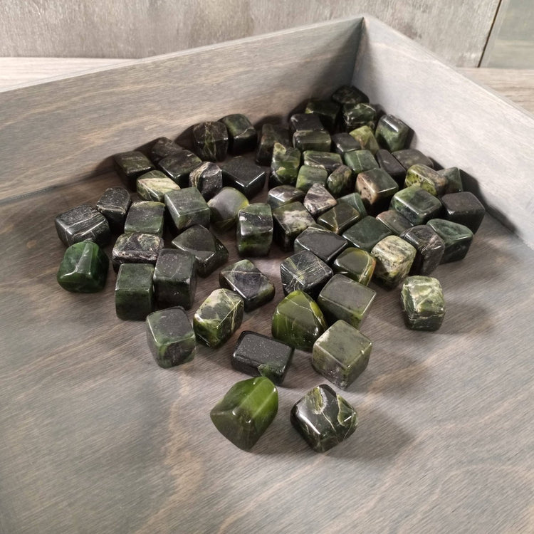 Green and black stones in a wooden box on a wooden surface
