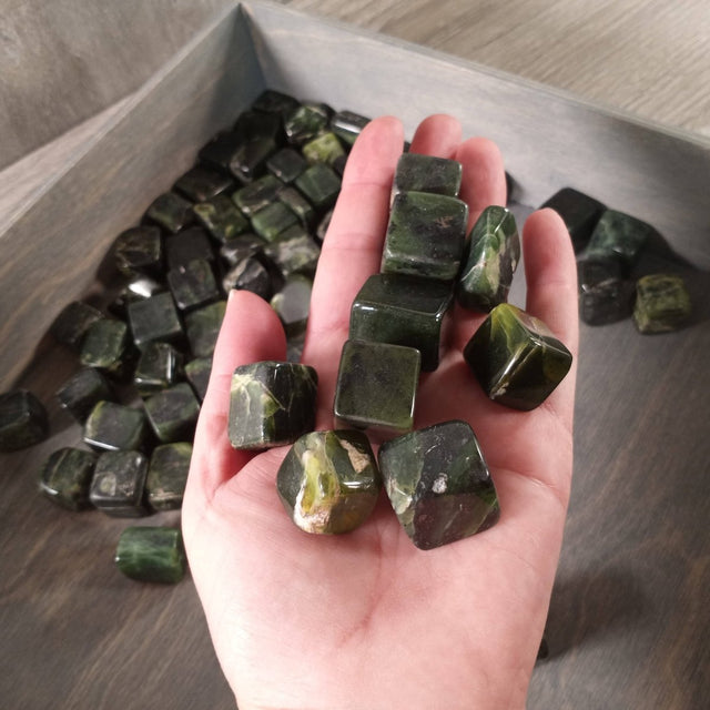 Hand holding green crystals with a tray of crystals in the background