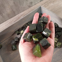 Hand holding green crystals with a tray of more crystals in the background