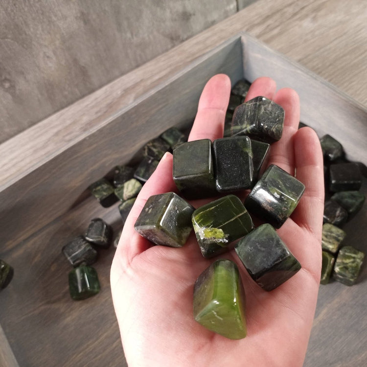 Hand holding green crystals with a tray of more crystals in the background