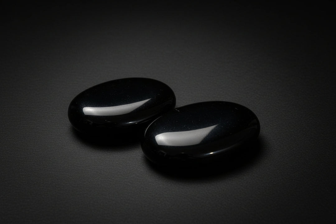Two polished black obsidian palm stones held in a hand