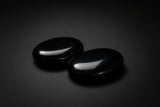 Two polished black obsidian palm stones held in a hand