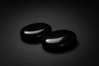 Two polished black obsidian palm stones held in a hand