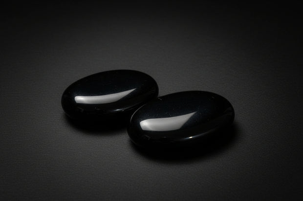 Two polished black obsidian palm stones held in a hand