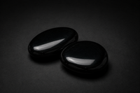 Two polished jet-black Obsidian palm stones with glossy reflections on a matte black surface