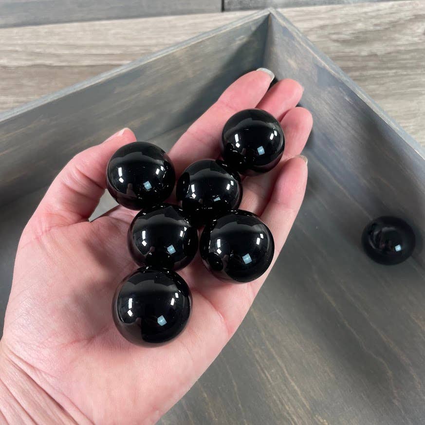 Hand holding six glossy black spheres on a wooden surface