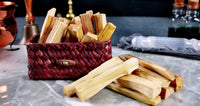 A basket filled with light-colored Palo Santo sticks on a marble surface, with a few sticks scattered outside the basket.