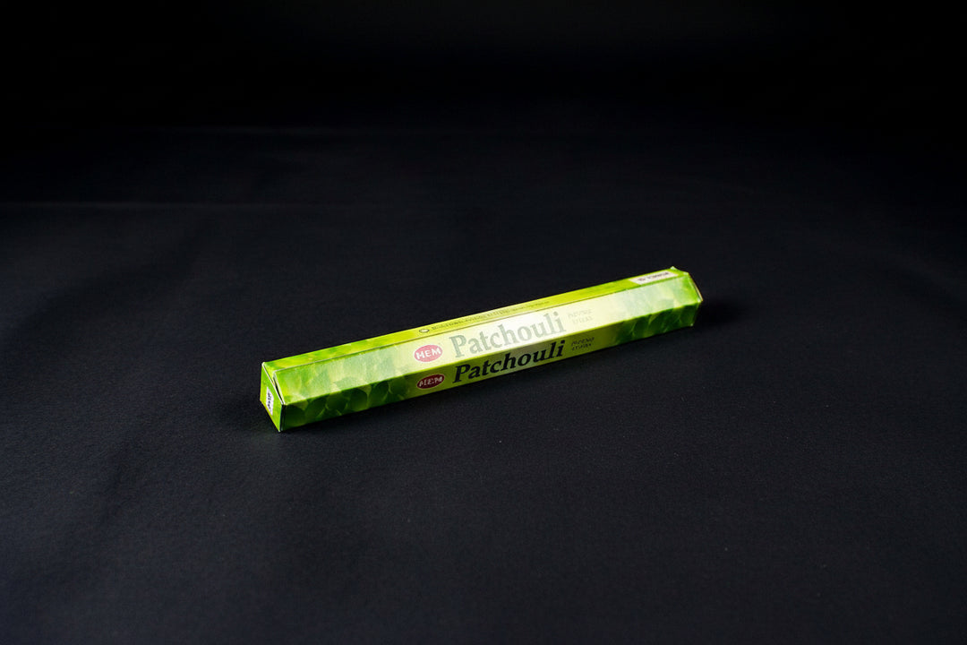 A pack of Patchouli incense sticks placed on a cloth beside a wooden box, with the name &