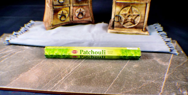 A pack of Patchouli incense sticks placed on a cloth beside a wooden box, with the name 'Patchouli' visible on the packaging.