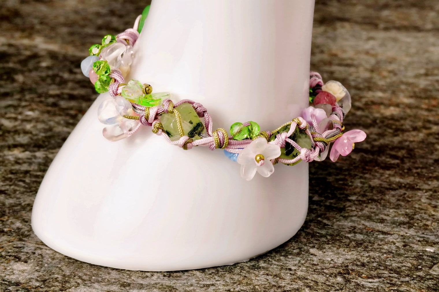 A beaded bracelet featuring natural pebbles and delicate flower beads, displayed on a white stand against a wooden background.