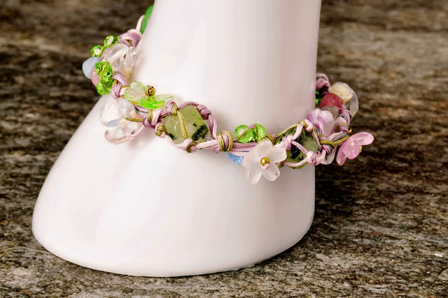 A beaded bracelet featuring natural pebbles and delicate flower beads, displayed on a white stand against a wooden background.
