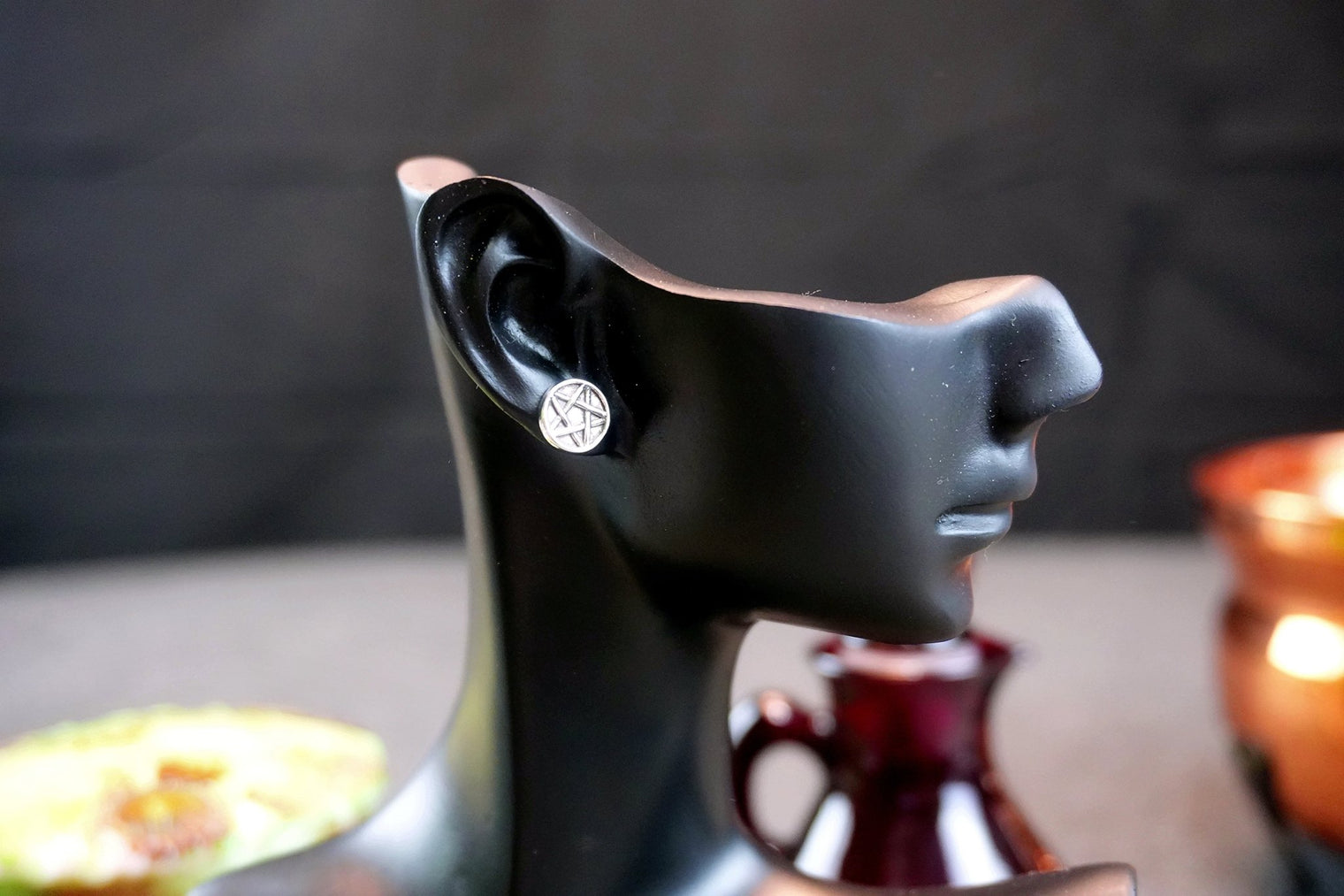 Black earring holder shaped like a face with an earring on a blurred background