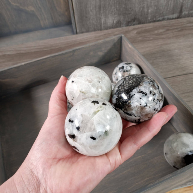 Hand holding three marbled rainbow moonstone spheres with a wooden tray in the background