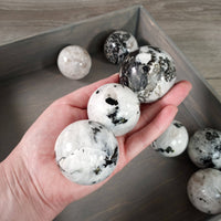 Hand holding marble-like spherical objects with a wooden tray in the background