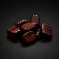 Seven polished red-brown tiger eye tumbled stones with dark chatoyant bands on a matte black surface