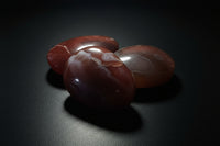 Three polished red and white agate stones arranged on a dark surface against a dark gray background.