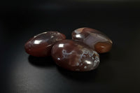 Three polished agate stones with natural banding in reddish-brown, orange, and white, displayed on a dark surface against a dark gray background.