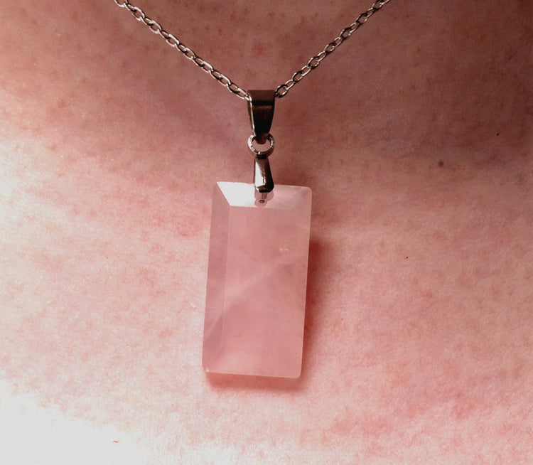 Pink rose quartz crystal pendant on a chain against a pink background
