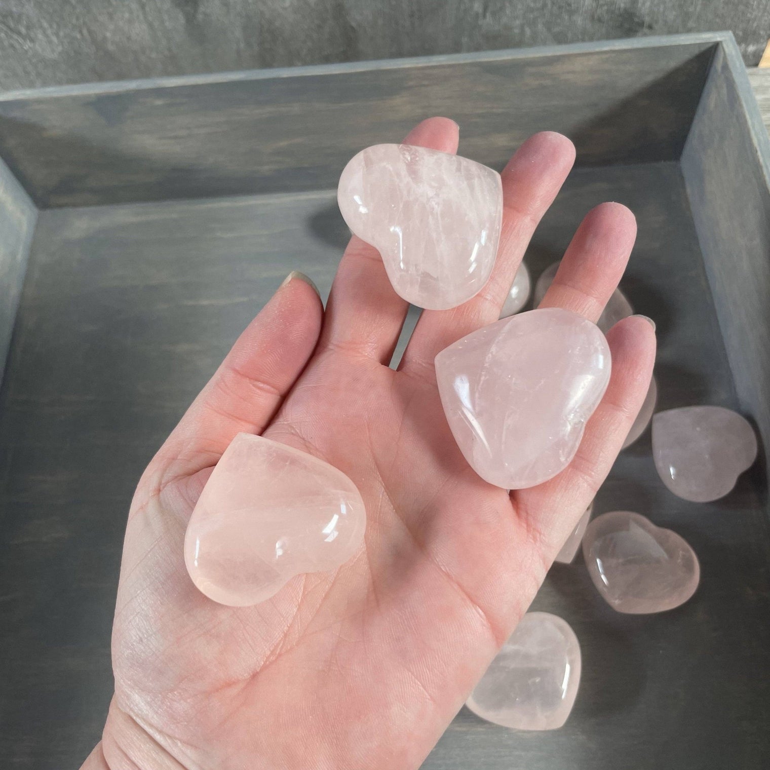 Hand holding heart-shaped rose quartz crystals with a metal container in the background