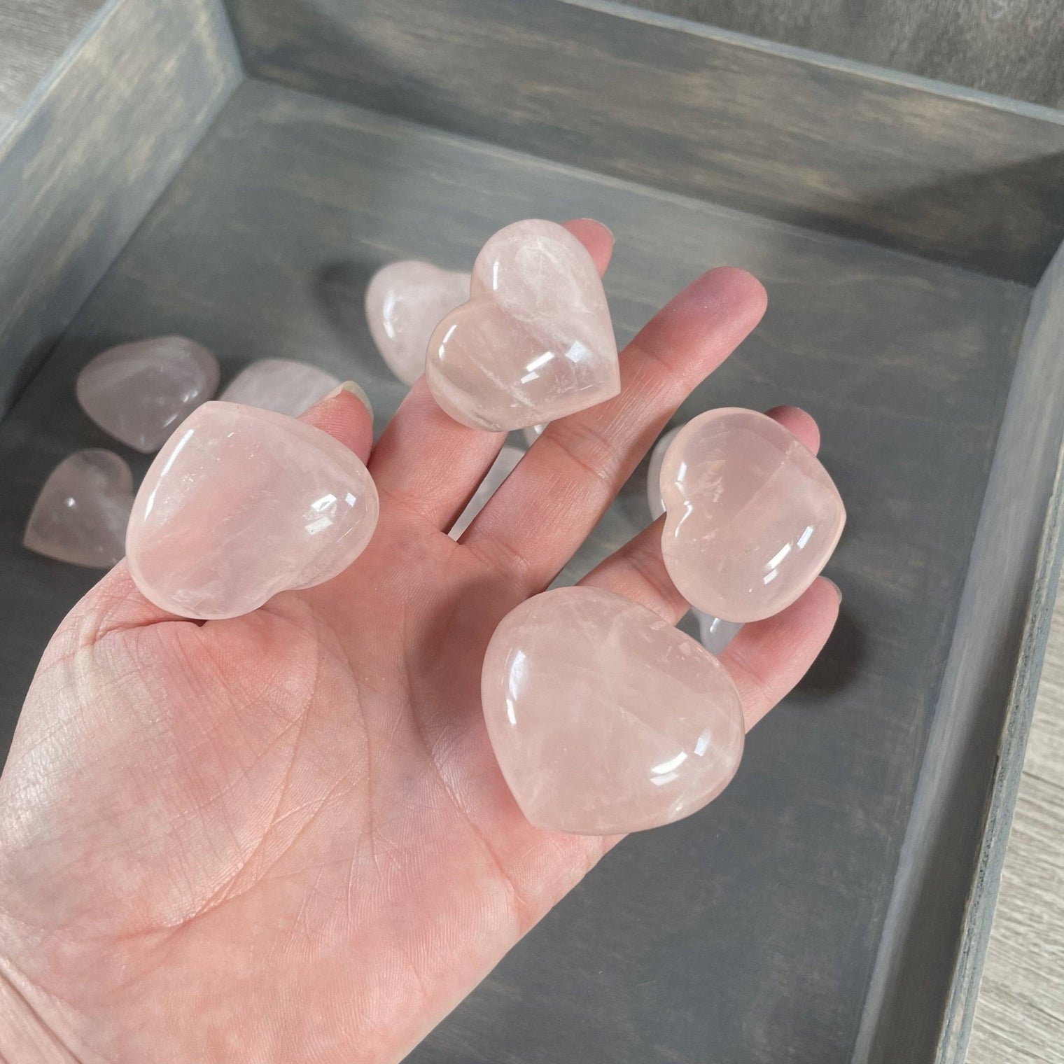 Hand holding heart-shaped rose quartz crystals with a neutral background