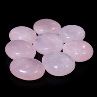 Eight polished pale pink rose quartz palm stones arranged on a black background