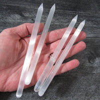 Clear crystal sticks held in a hand against a wooden background