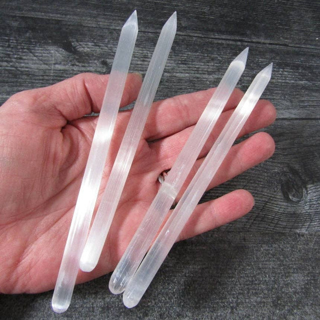 Clear crystal sticks held in a hand against a wooden background