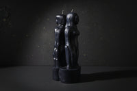 Black candle holders shaped like abstract human figures on a dark background with 