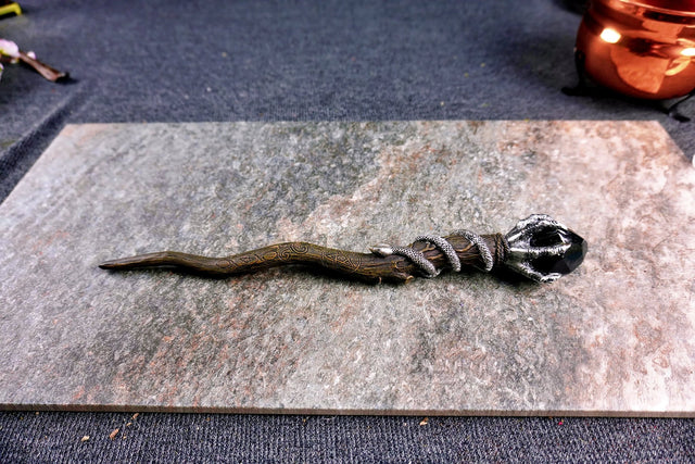A 13-inch crooked wand shaped like natural wood with a serpent wrapped around the handle and an eagle on top holding a black jewel.