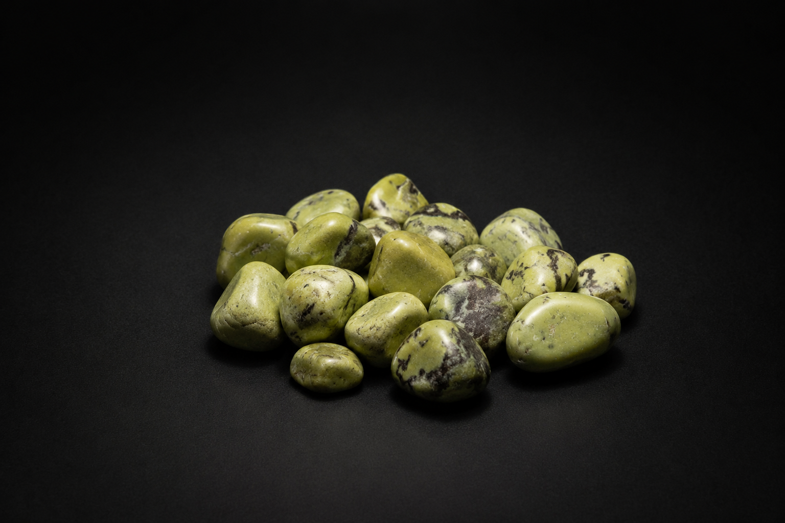 Assortment of polished olive and yellow-green Serpentine tumbled stones with dark mottling on black