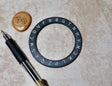 Circular object with lettering, pen, and cookie on a beige surface