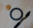 Black lettering ring, small round object, and pen on a textured surface