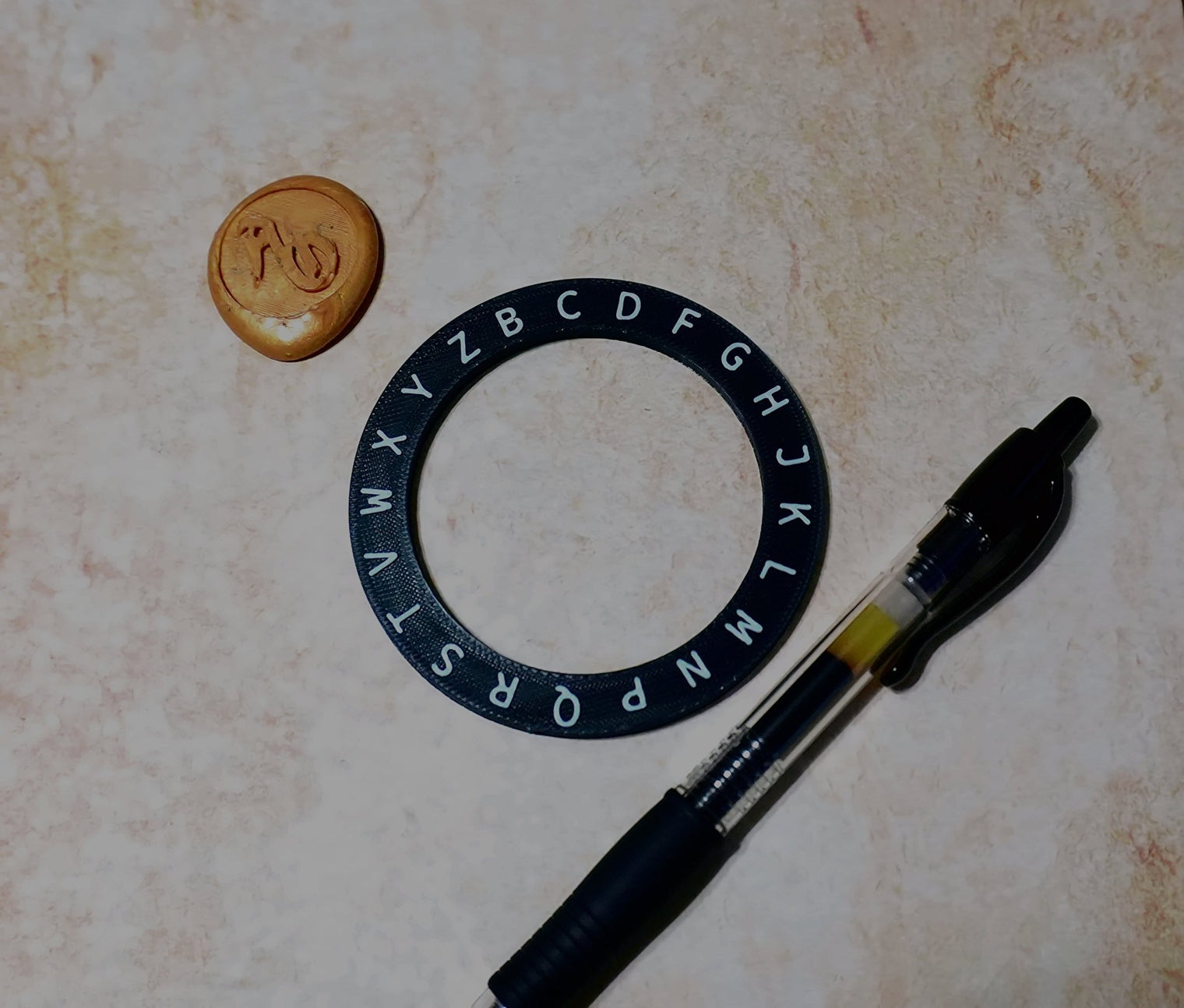 Black lettering ring, small round object, and pen on a textured surface