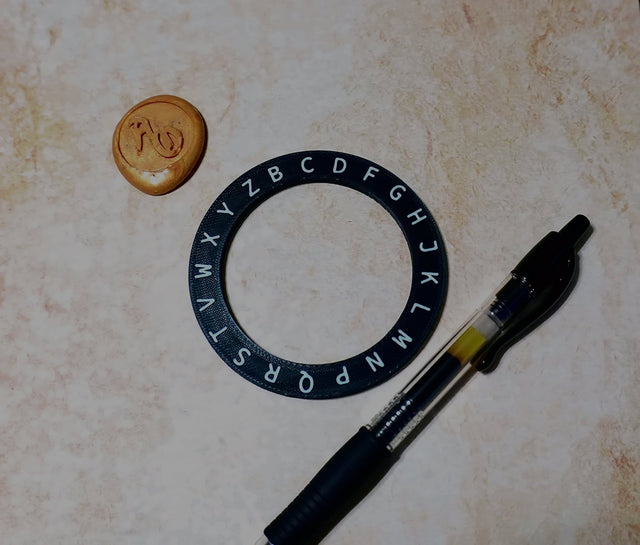 Black lettering ring, small round object, and pen on a textured surface